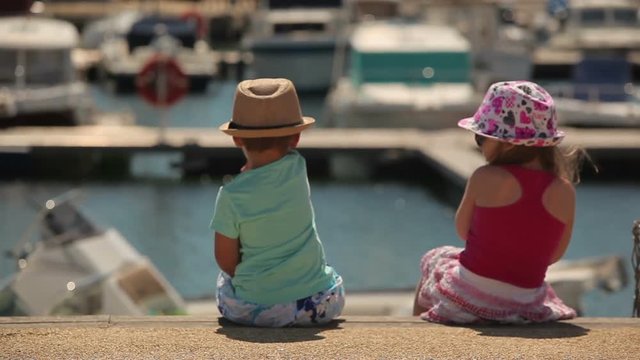 Little boy and girl sitting on a pier Yacht Club