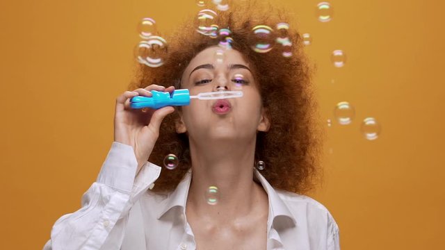 Funny fashion girl blowing soap bubbles on orange background. Close up. Slow motion