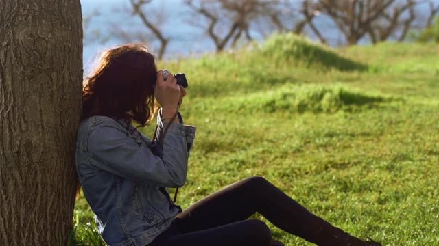 Beautiful brunette photographer sitting near the tree in park. Close up. Slow motion