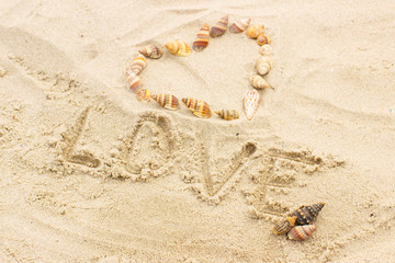 Word love written on sand at the beach, heart of shells