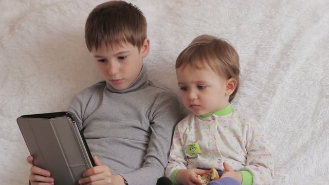 Children sitting on the couch playing on your tablet and phone to computer games