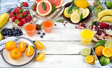 Citrus juice, fruits and berries on white wooden background.