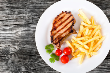 grilled pork chops on a white dish with french fries