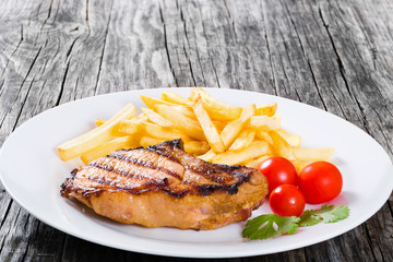 grilled pork chops on a white dish with french fries