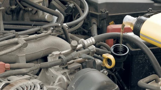 Auto mechanic pours additional motor engine oil into the car. Vehicle service and maintenance scene. 4K UHD video footage.