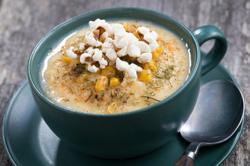 corn soup with popcorn in ceramic cup on wooden table, closeup