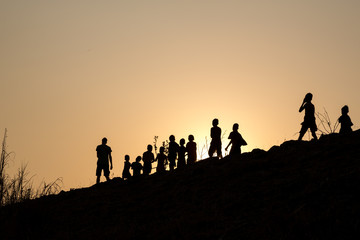 Fototapeta na wymiar silhouette row of children walking along with young man in the wonderful orange sunset