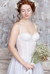 Naklejka premium Beautiful red-haired bride with bouquet of wild flowers. She has a perfect pale skin and delicate blush. White flowers in her hair. She smiles gently. Her eyes are closed.