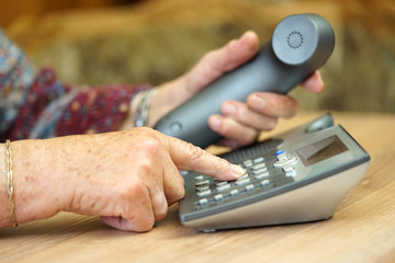 closeup of old female hands dialing a telephone number