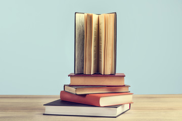 Libros apilados sobre una mesa de madera y un fondo celeste pastel. Vista de frente y de cerca....