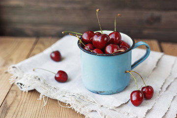 Fresh juicy sweet cherries  in old rusty mug. Rustic wooden background with homespun napkin.