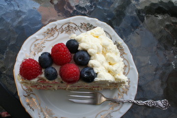 Piece of gateau with blueberry, raspberry and cream on top, strawberry and vanilla cream inside