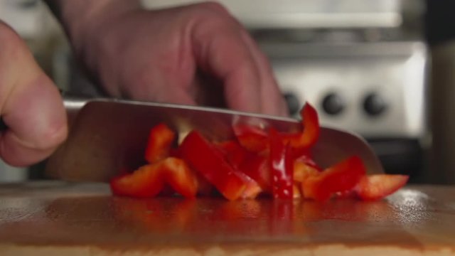 SLOW: A cook's hand cuts a bell pepper by a knife on a cutting board