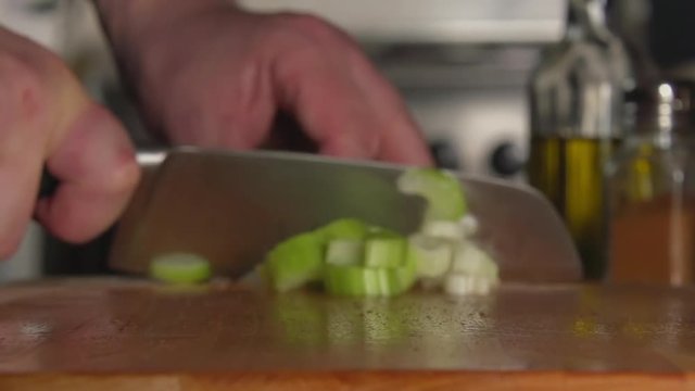 SLOW: A cook's hand cuts a celery by a knife on a cutting board