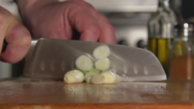 SLOW: A cook's hand cuts a green onion by a knife on a cutting board