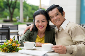 Happy senior Asian couple enjoying cappuccino in cafe