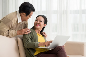 Smiling mature woman discussing something on laptop with her husband
