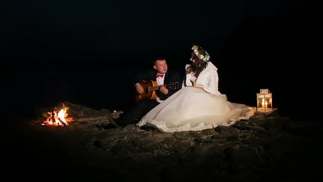 groom playing guitar in the night at campfire