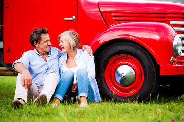 Senior couple sitting at the red vintage car © Halfpoint