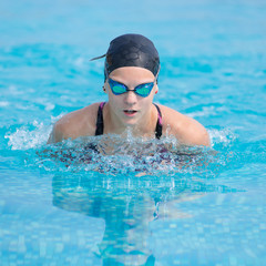 Fototapeta na wymiar Young girl in goggles and cap swimming butterfly stroke style in the blue water pool