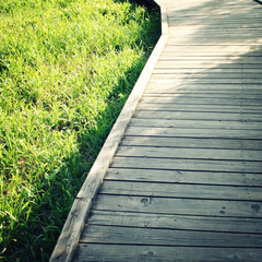 Fototapeta premium Wooden path in a spring park. Aged photo. Footpath photo with copy space area. Wooden pathway in the forest. Outdoors. Toned photo.