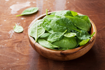 Baby spinach leaves in wooden bowl on old rustic table, organic food