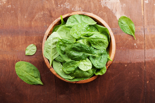 Baby spinach leaves in wooden bowl on old rustic table, organic food, top view