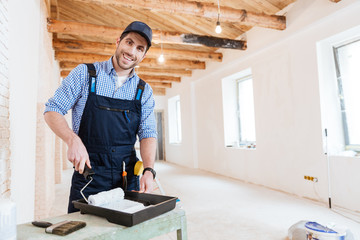 Smiling builder using paint roller indoors