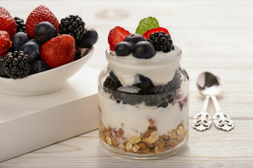 Healthy yogurt dessert with muesli, strawberries, blackberries and  blueberries on white wooden table.
