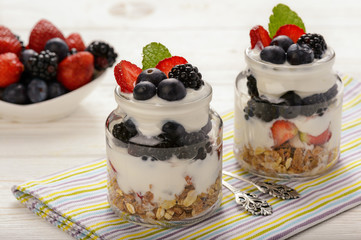 Healthy yogurt dessert with muesli, strawberries, blackberries and  blueberries on white wooden table.