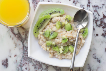 Bowl of oatmeal porridge with kiwi on marble table