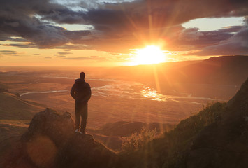 Man standing on a ledge of a mountain, enjoying the beautiful sunset over a wide river valley in Thorsmork, Iceland.