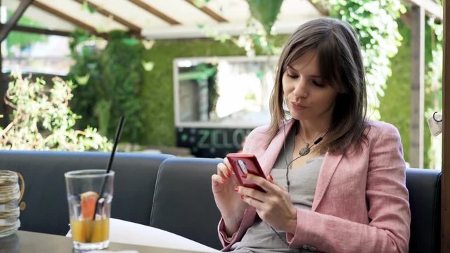 Sad, pensive woman listening to music on cellphone in cafe in garden

