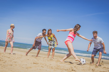 Group of multiracial friends playing football at the beach