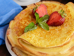 Pile of golden pancakes with strawberries and strawberry jam, decorative sprig of mint. Close-up