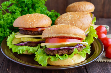 Many hamburgers at home (bun, tomato, cucumber, onion rings, lettuce, pork chops, cheese) in a clay bowl on a wooden background. Close-up