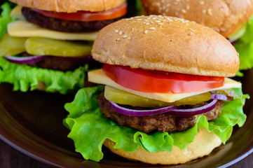 Hamburgers at home (bun, tomato, cucumber, onion rings, lettuce, pork chops, cheese) in a clay bowl on a wooden background. Close-up