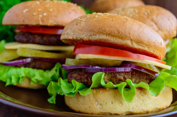 Hamburgers at home (bun, tomato, cucumber, onion rings, lettuce, pork chops, cheese) in a clay bowl on a wooden background. Close-up