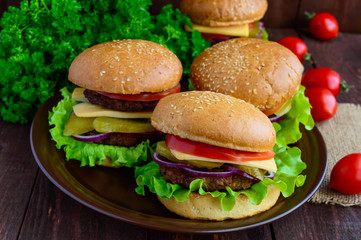 Hamburgers at home (bun, tomato, cucumber, onion rings, lettuce, pork chops, cheese) in a clay bowl on a wooden background. Close-up