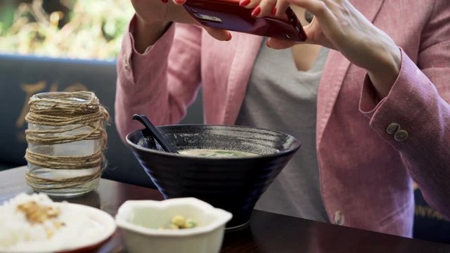 Woman taking photo of soup with cellphone sitting in cafe in garden
