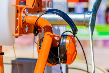 Orange hearing protections or earmuffs hanging on an orange machine part.