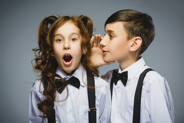 Teenage boy whispering in the ear of teen girl on a gray background. Positive human emotion, facial expression. Closeup. Communication concept