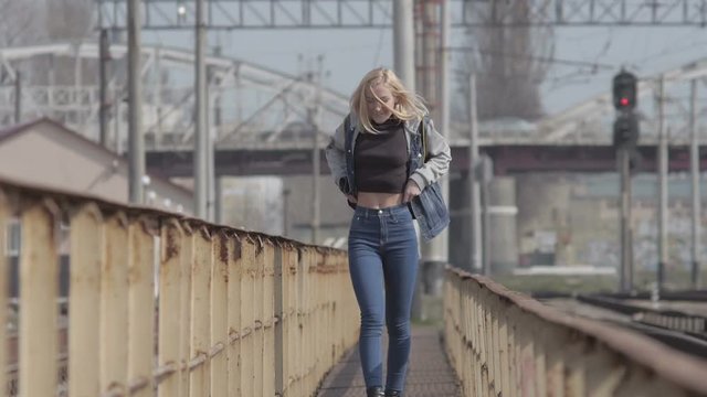 Young pretty girl walking on the railway and takes of jeans jacket