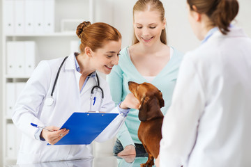 happy woman with dog and doctor at vet clinic