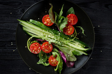 Healthy food. Fresh Salad with arugula and tomatoes on black background, top view