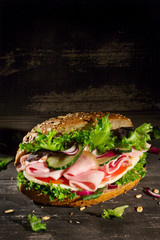 Sandwich with vegetables, ham and cheese on dark wood background, upright