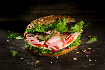 Sandwich with vegetables, ham and cheese on dark wood background