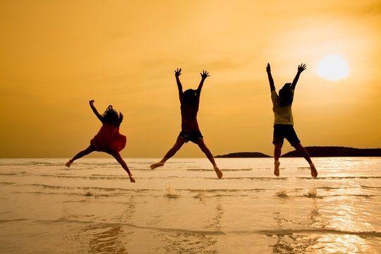 Silhouette of 3 little asian girls jumping on beach in sunset