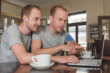 smiling gay couple doing online banking on their laptop