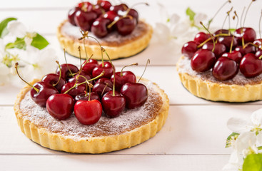 Tarts with almond stuffing and sweet cherry on a white wooden background with flowering branches of apple trees 